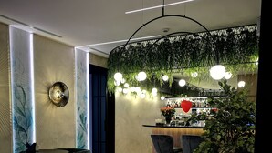A modern dining area with a round table, black chairs, and a bar counter with a green wall and hanging lights. - Amrita Hotel (Liepaja)