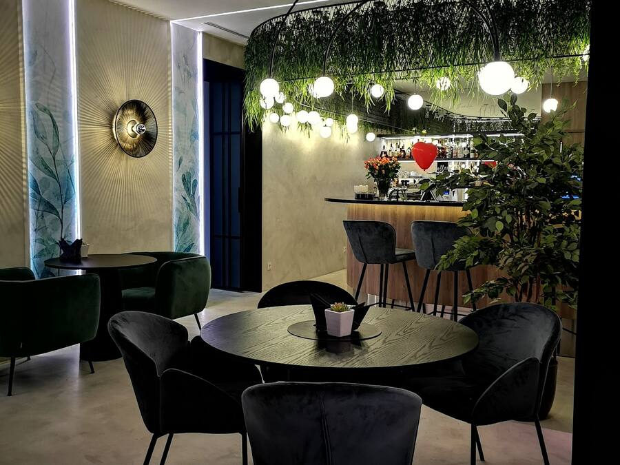 Un área de comedor moderna con una mesa redonda, sillas negras y una barra con pared verde y luces colgantes.