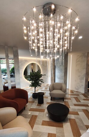A modern interior with a central chandelier, a round mirror, and a potted plant. - Amrita Hotel (Liepaja)