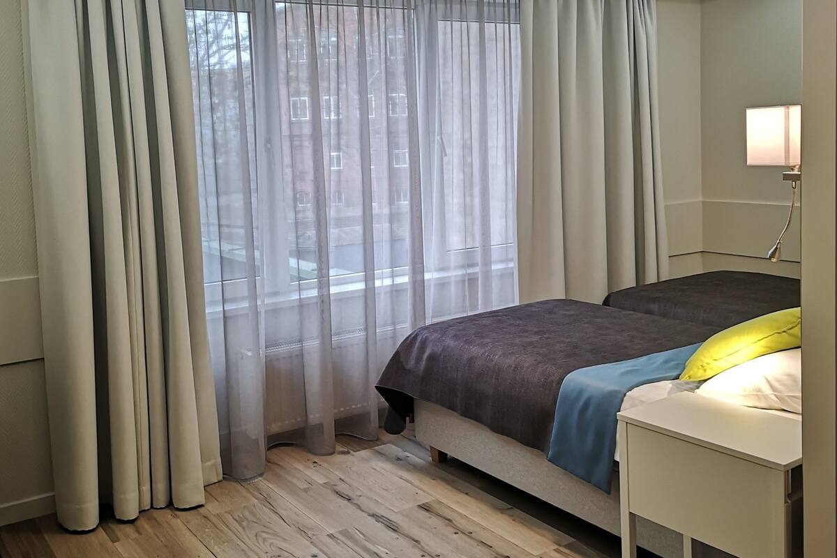Un dormitorio moderno con una cama, una mesita de noche y una ventana con cortinas traslúcidas.
