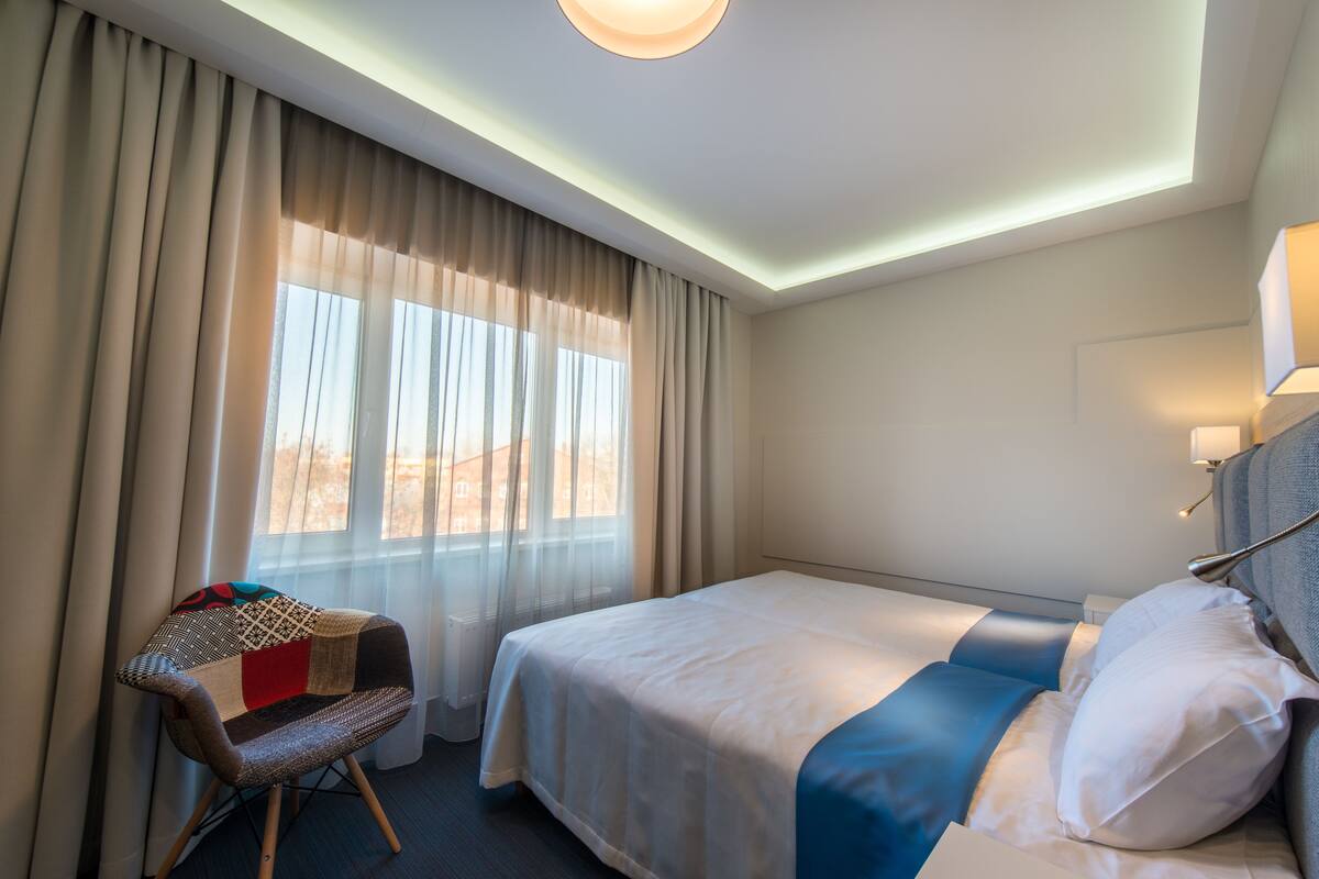 Una habitación de hotel con cama, una silla y ventana con cortinas.