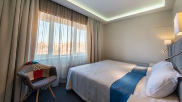 Habitació d'hotel amb un llit, una cadira i una finestra amb cortines.