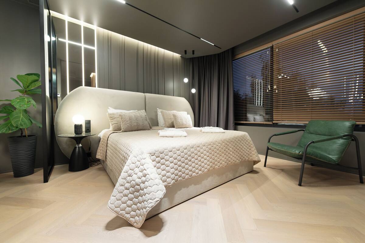 Un dormitorio moderno con una cama grande, mesitas de noche, una silla verde y una planta en maceta.