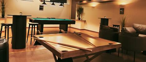 Una mesa de billar en una sala con una mesa de pool, un reloj en la pared y un sofá.