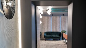 A modern interior with a herringbone floor, a dark green sofa, and a wall-mounted fan. - Amrita Hotel (Liepaja)