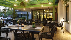 An outdoor dining area with tables and chairs, a green ceiling, and hanging plants. - Amrita Hotel (Liepaja)