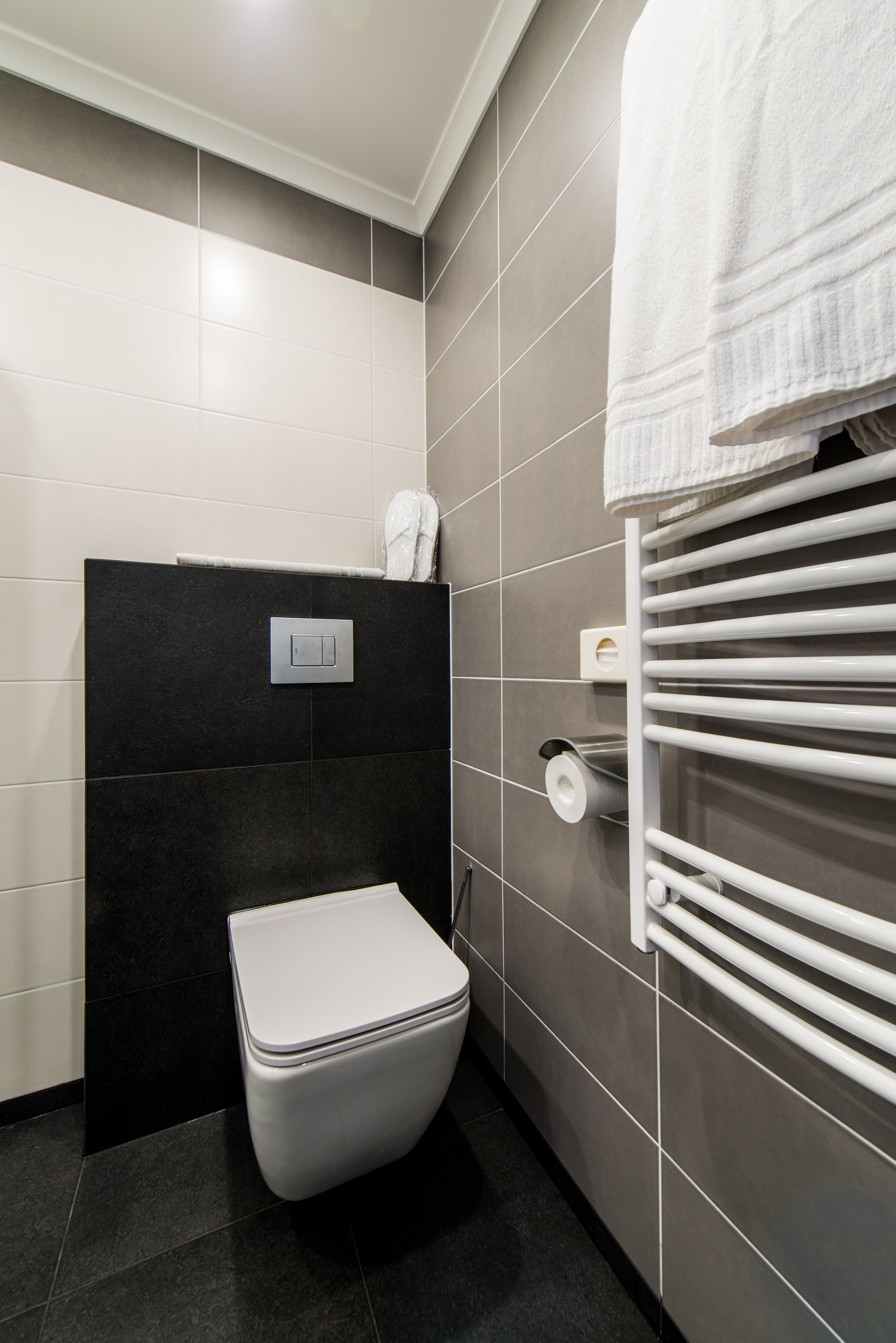 A modern bathroom with a toilet, towel rack, and a wall-mounted toilet paper holder.