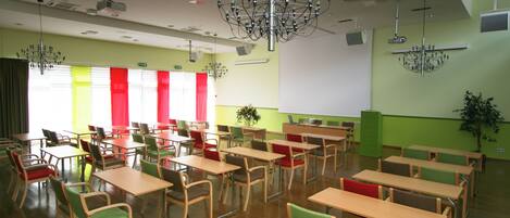 A classroom with multiple tables and chairs, a projector, and a screen.