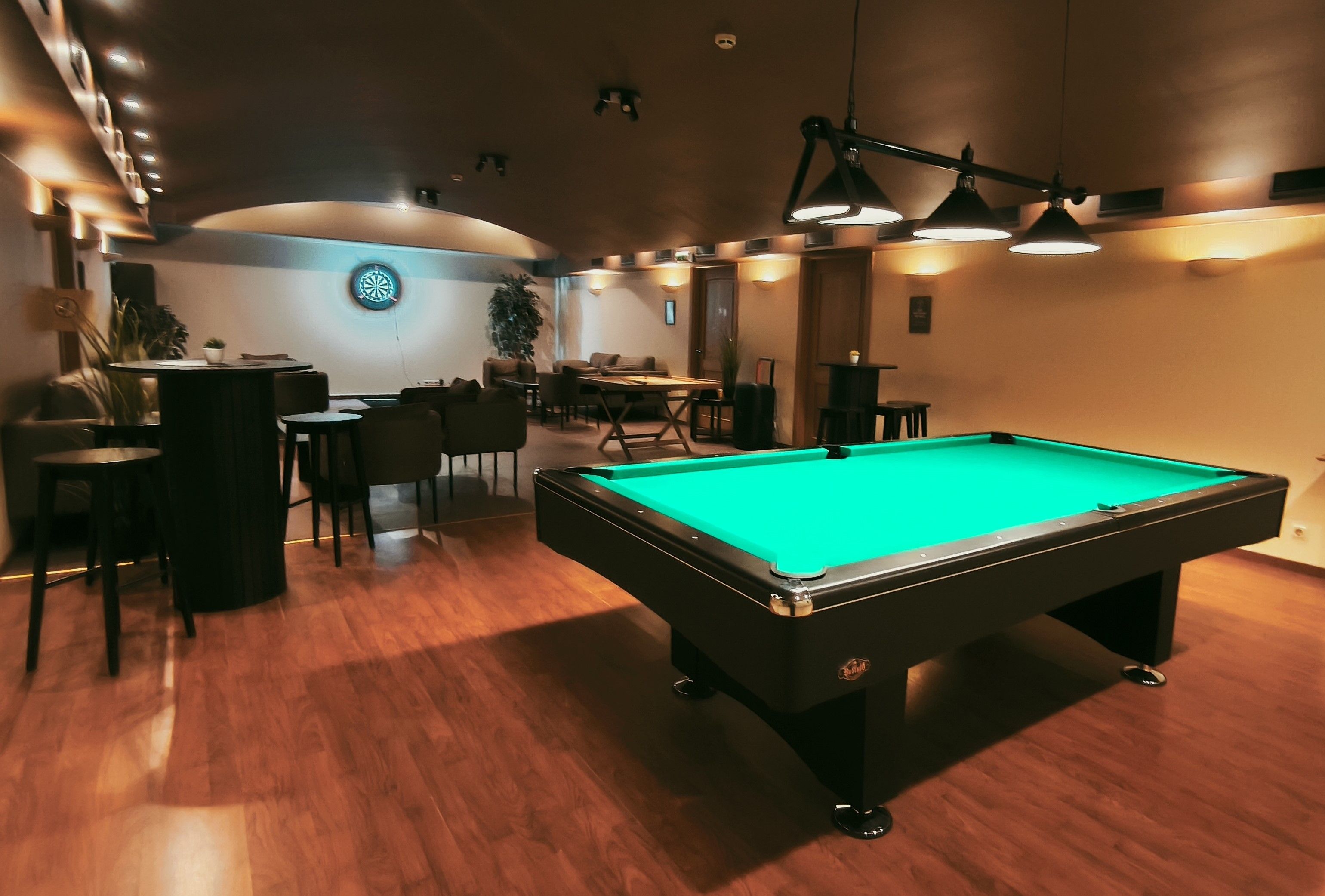 Una sala de billar con mesa de billar, sillas y dardos.