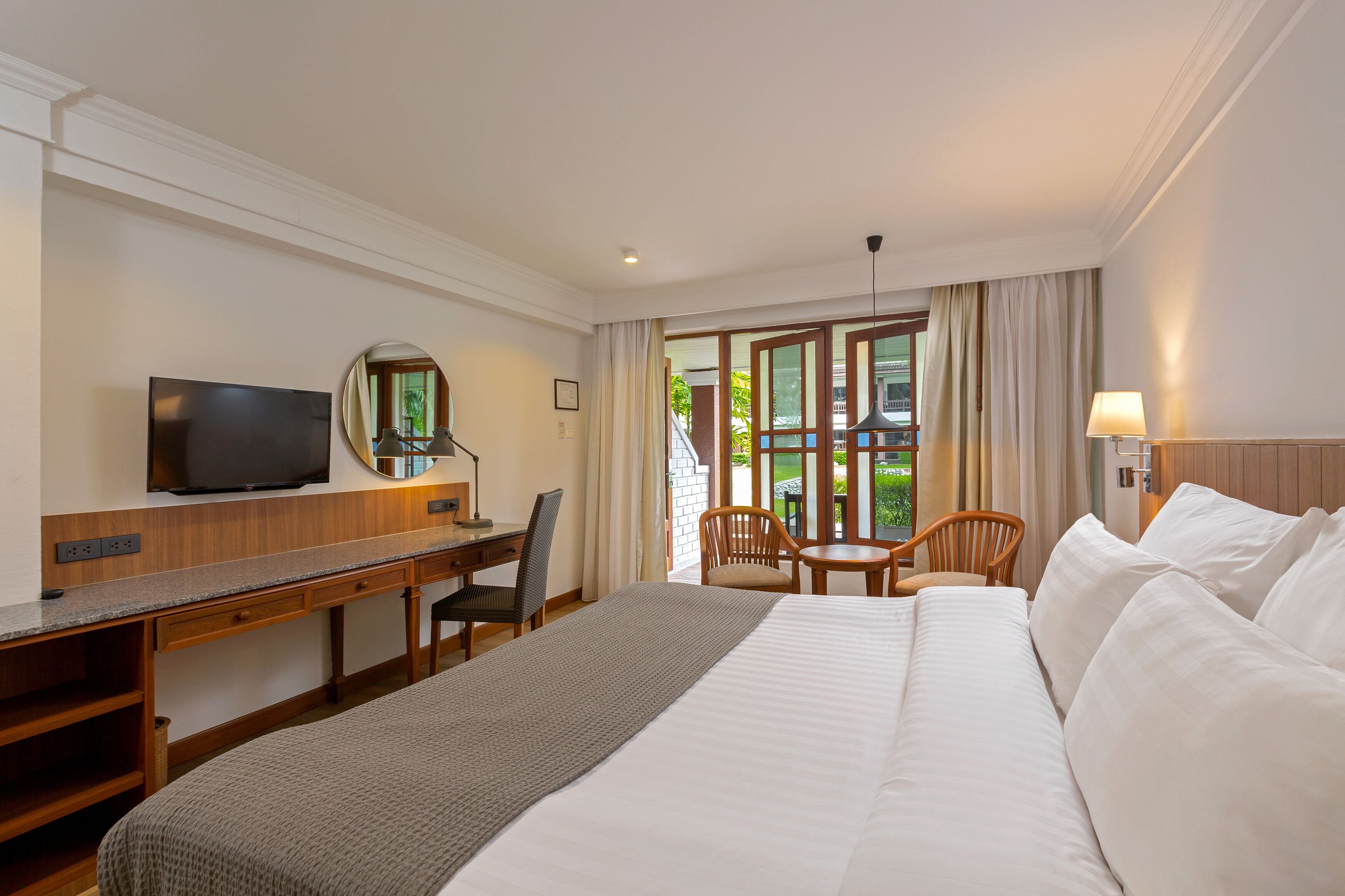 A hotel room with a bed, desk, TV, and a view of the outdoors.