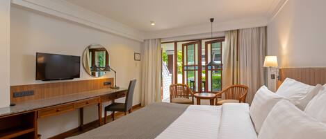 A hotel room with a bed, desk, TV, and a view of the outdoors.