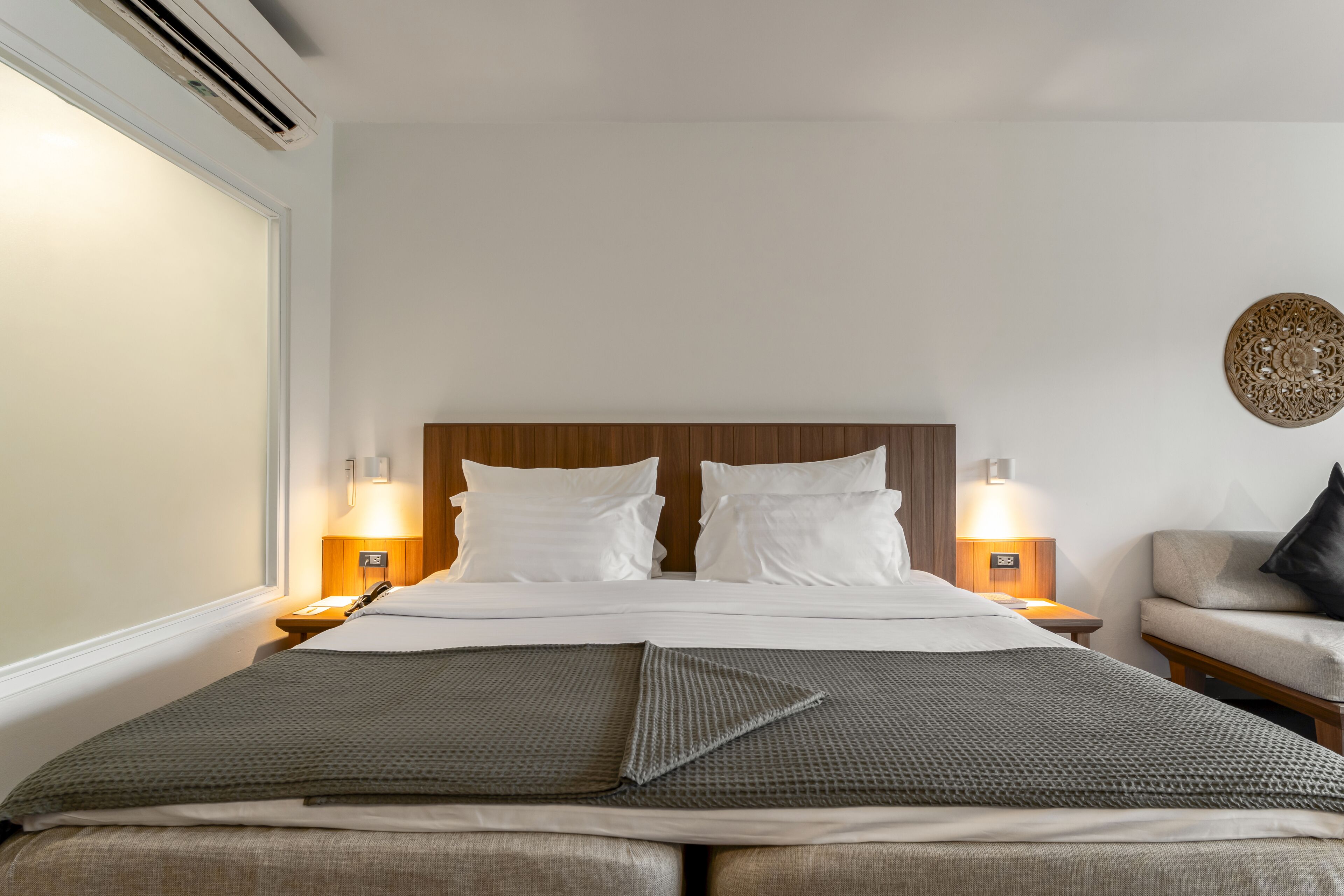 A neatly made bed with white linens, two bedside lamps, a wooden headboard, and a grey throw blanket.