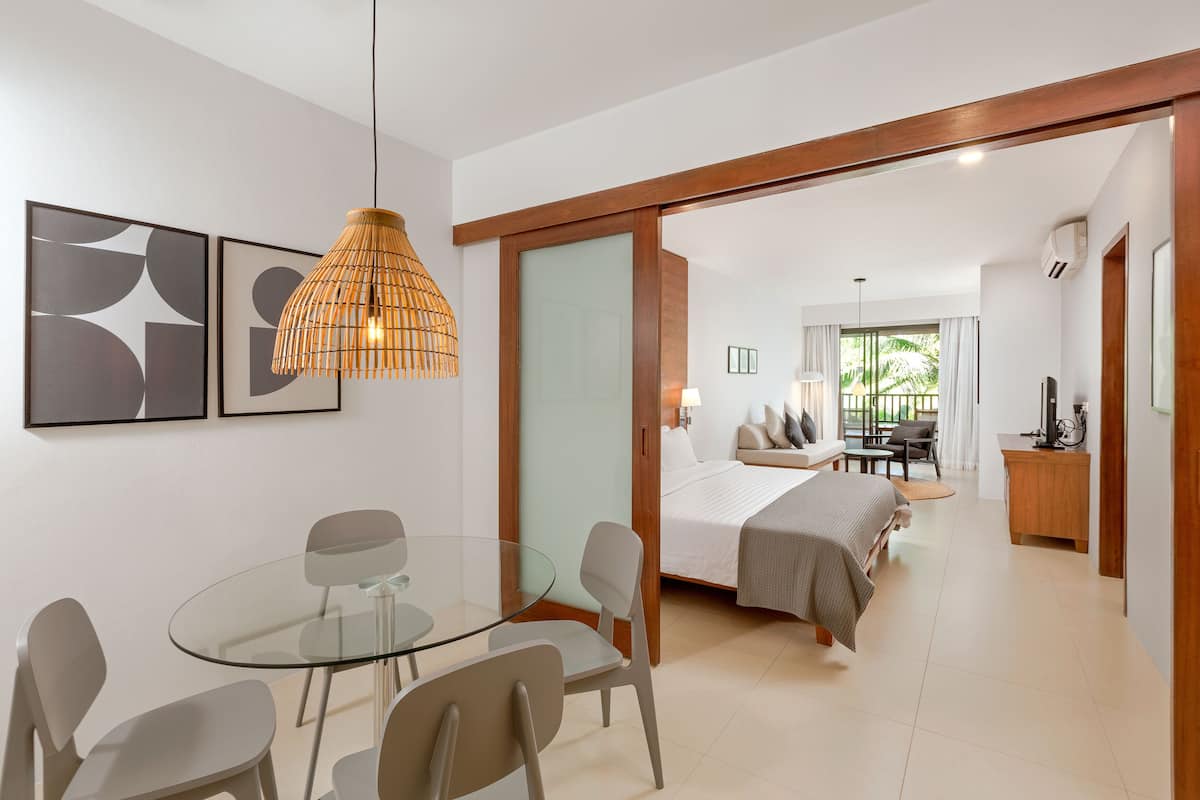 A modern hotel room with a glass dining table, a bed with a view, and a wooden-framed sliding door.