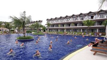 A swimming pool with people in the water, surrounded by lounge chairs and palm trees.