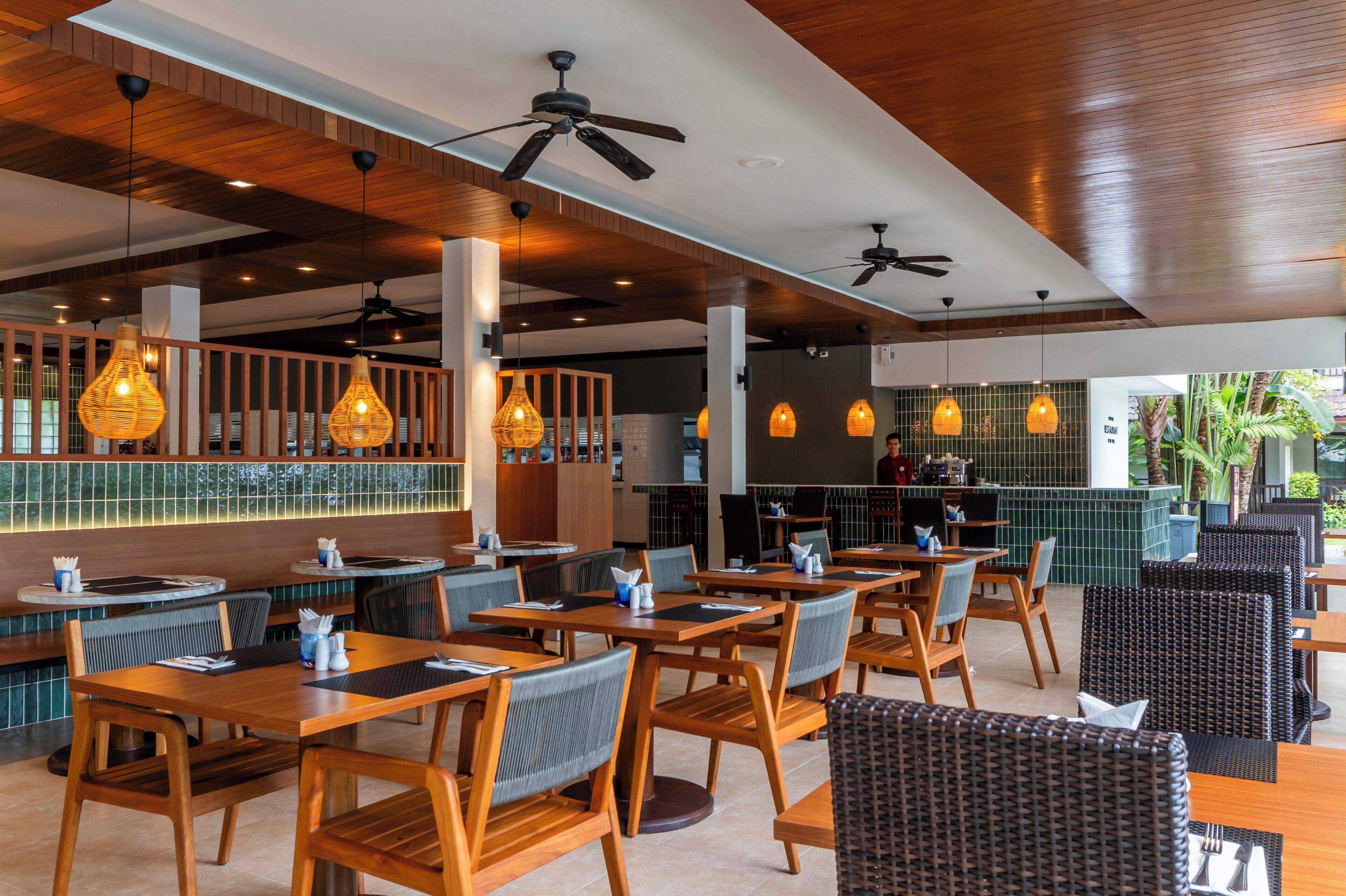 A restaurant with wooden tables and chairs, hanging pendant lights, and ceiling fans.