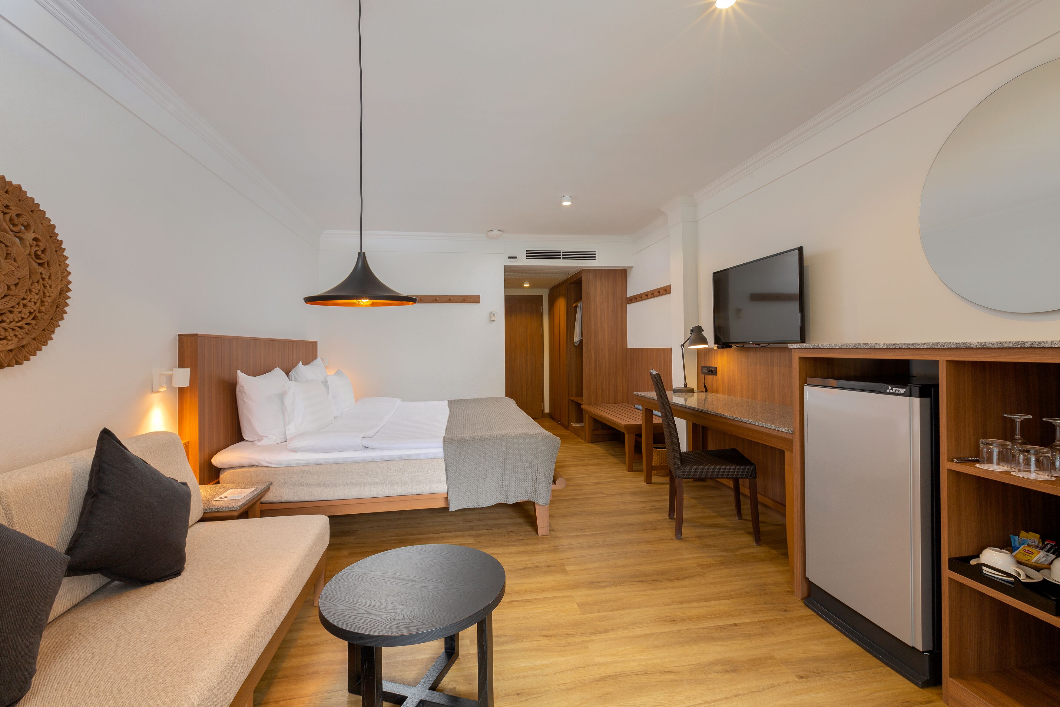 A compact hotel room with a bed, a sofa, a dining table, a TV, and a refrigerator.