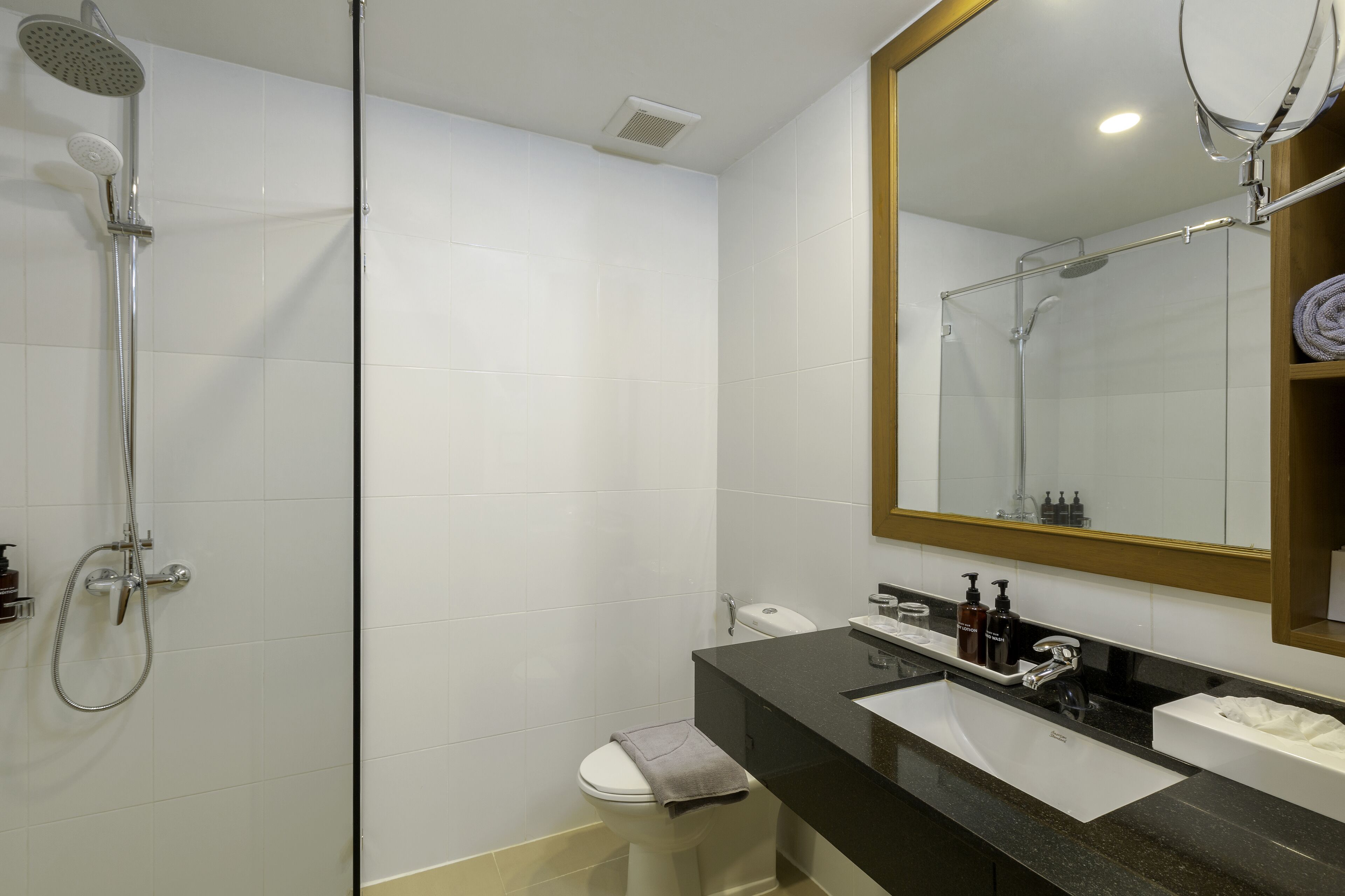 A modern bathroom with a glass-enclosed shower, a white toilet, a black sink vanity, and a large mirror.