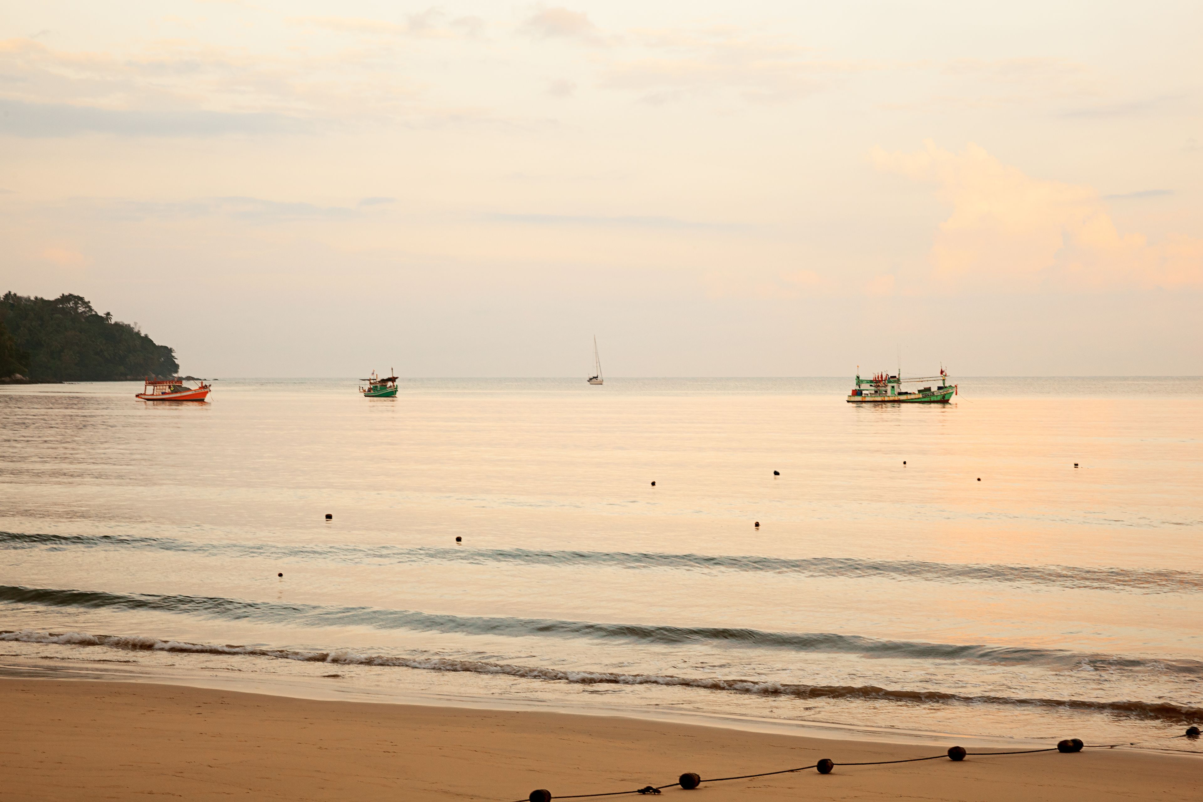 A beach with calm waters, boats, and a distant shoreline.