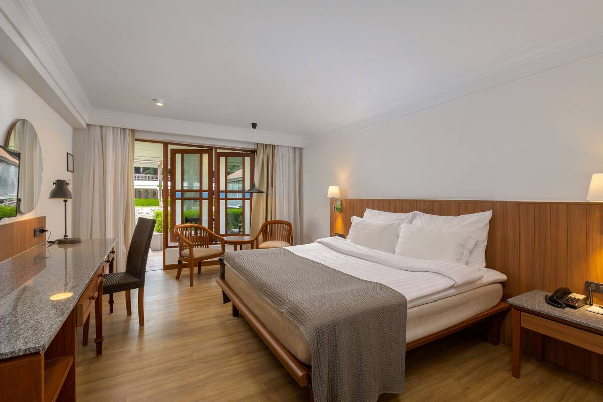 A hotel room with a large bed, a desk with a lamp, a chair, and a nightstand with a phone.