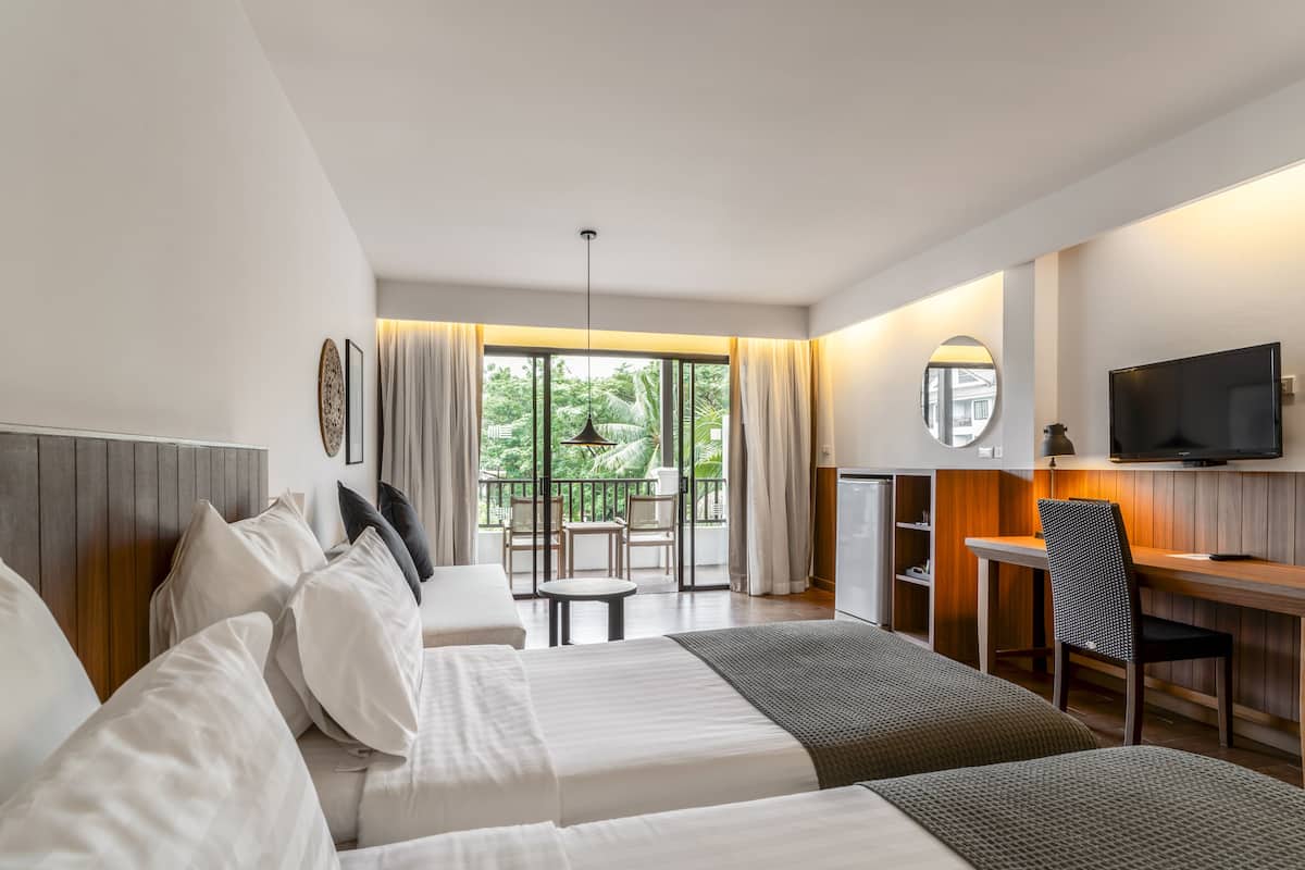 A hotel room with a bed, a desk, a TV, and a balcony with a view of greenery.