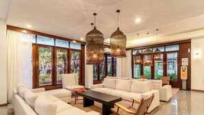 A spacious living area with a large sectional sofa, a coffee table, and wicker chairs. There are large windows with curtains, and a digital thermostat on the wall. - Sunprime Kamala Beach (Kamala)