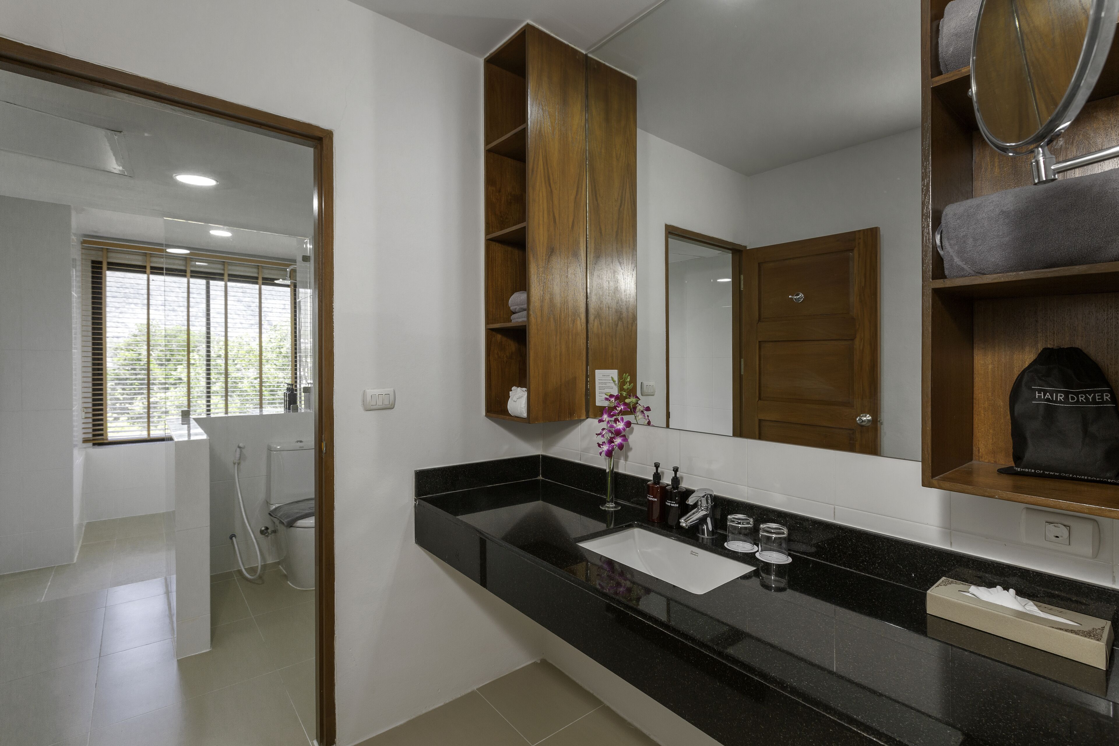A modern bathroom with a black countertop, a wooden vanity, a mirror, and a shower area.