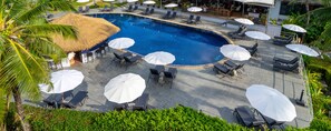 Piscina com espreguiçadeiras e guarda-sóis, cercada por vegetação.
