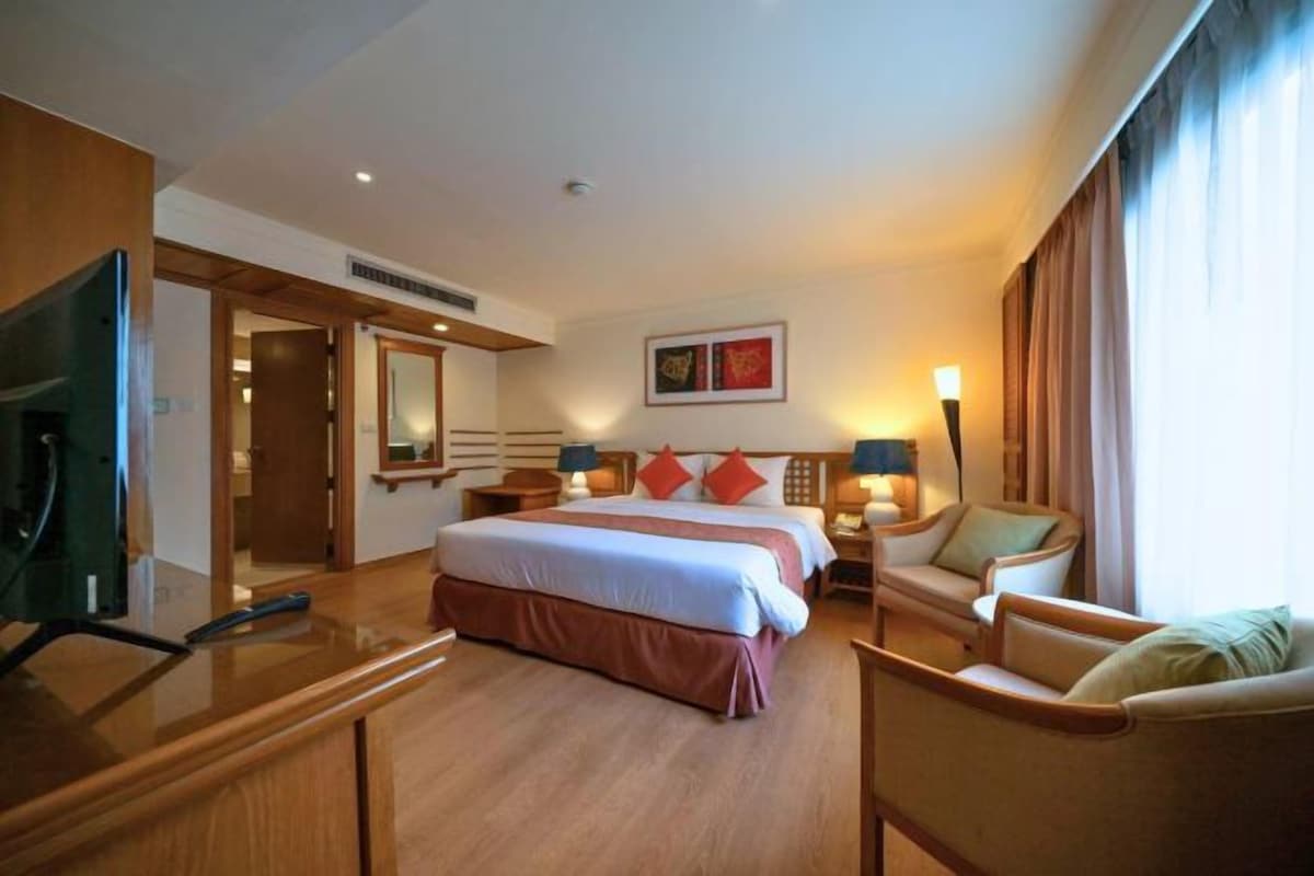 A hotel room with a large bed, two bedside tables with lamps, a TV, a chair, and a desk.