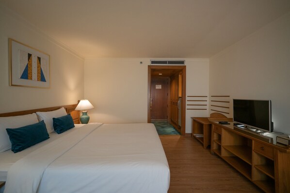 A hotel room with a large bed, a desk with a TV, a lamp, and a door leading to another room. - Silom Serene, a Boutique Hotel (Bangkok)