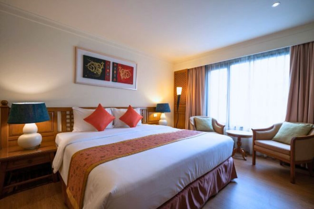 A hotel room with a large bed, two bedside lamps, a small table, and a chair.