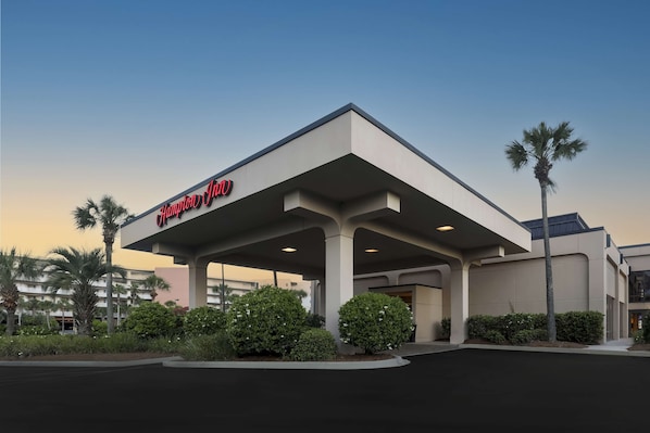 A Hampton Inn hotel with a modern design, featuring a covered parking area and well-maintained landscaping.