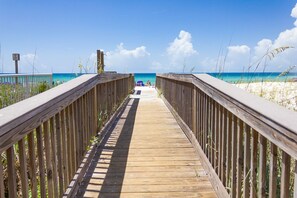 A wooden boardwalk leading to a beach with clear blue water and white sand.