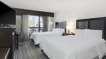 Habitación de hotel con dos camas, un escritorio, una silla y un balcón con vista a edificios.