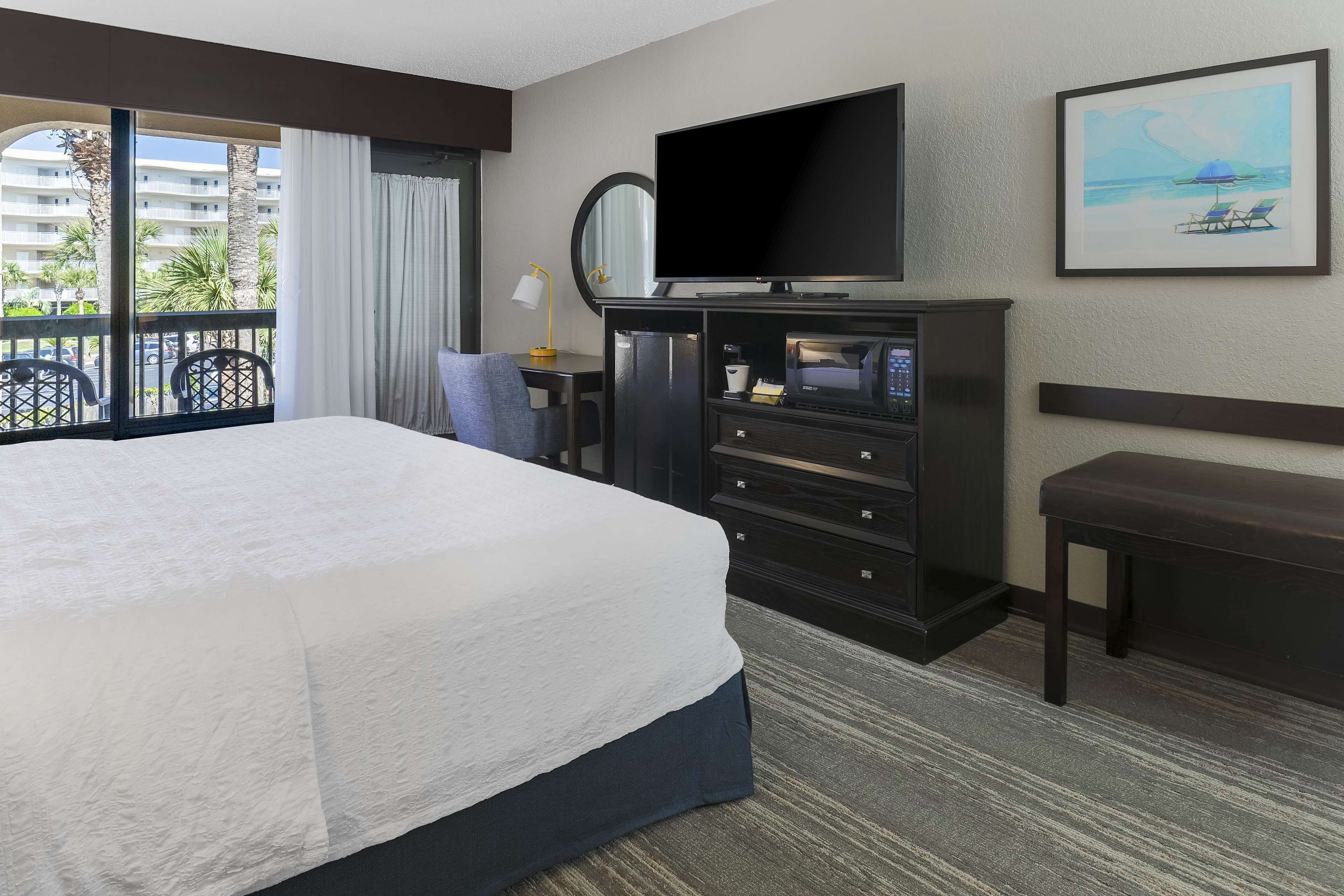 Habitación de hotel con una cama grande, televisor de pantalla plana, escritorio con lámpara, cafetera y vistas al exterior.