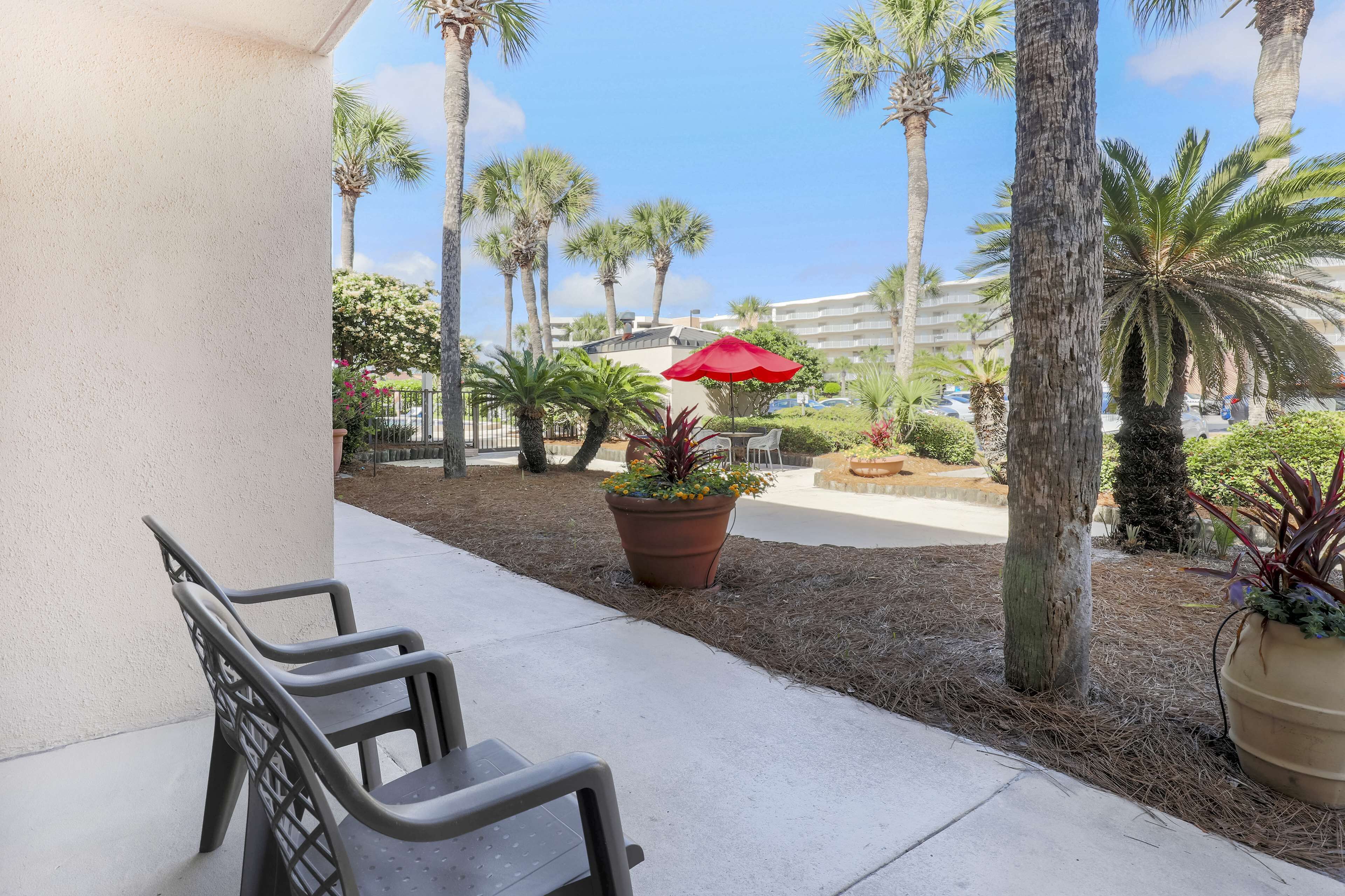 A patio area with outdoor seating, palm trees, and a red umbrella.