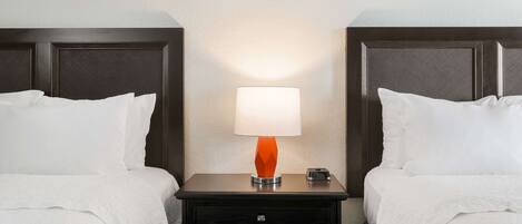 A hotel room with two beds, a nightstand with a lamp, and a small drawer.