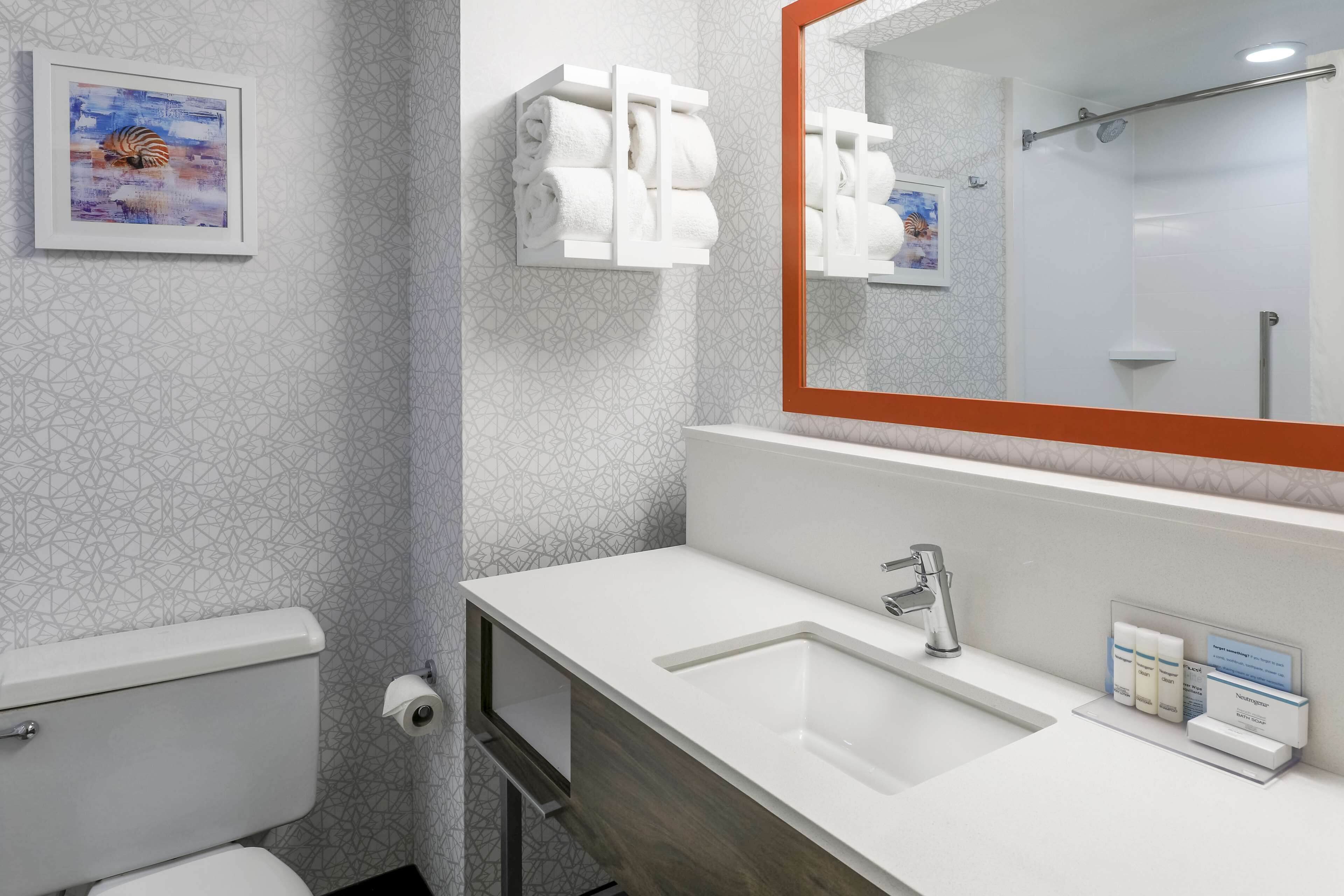 A modern bathroom with a white sink, a large mirror, and a toilet. There are towels and toiletries on the wall.