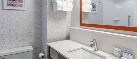 Une salle de bain moderne avec un lavabo blanc, un grand miroir et des toilettes. Des serviettes et des articles de toilette sont accrochés au mur.