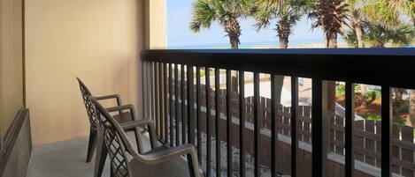 A balcony with two chairs, a wooden fence, and a view of palm trees and a beach.