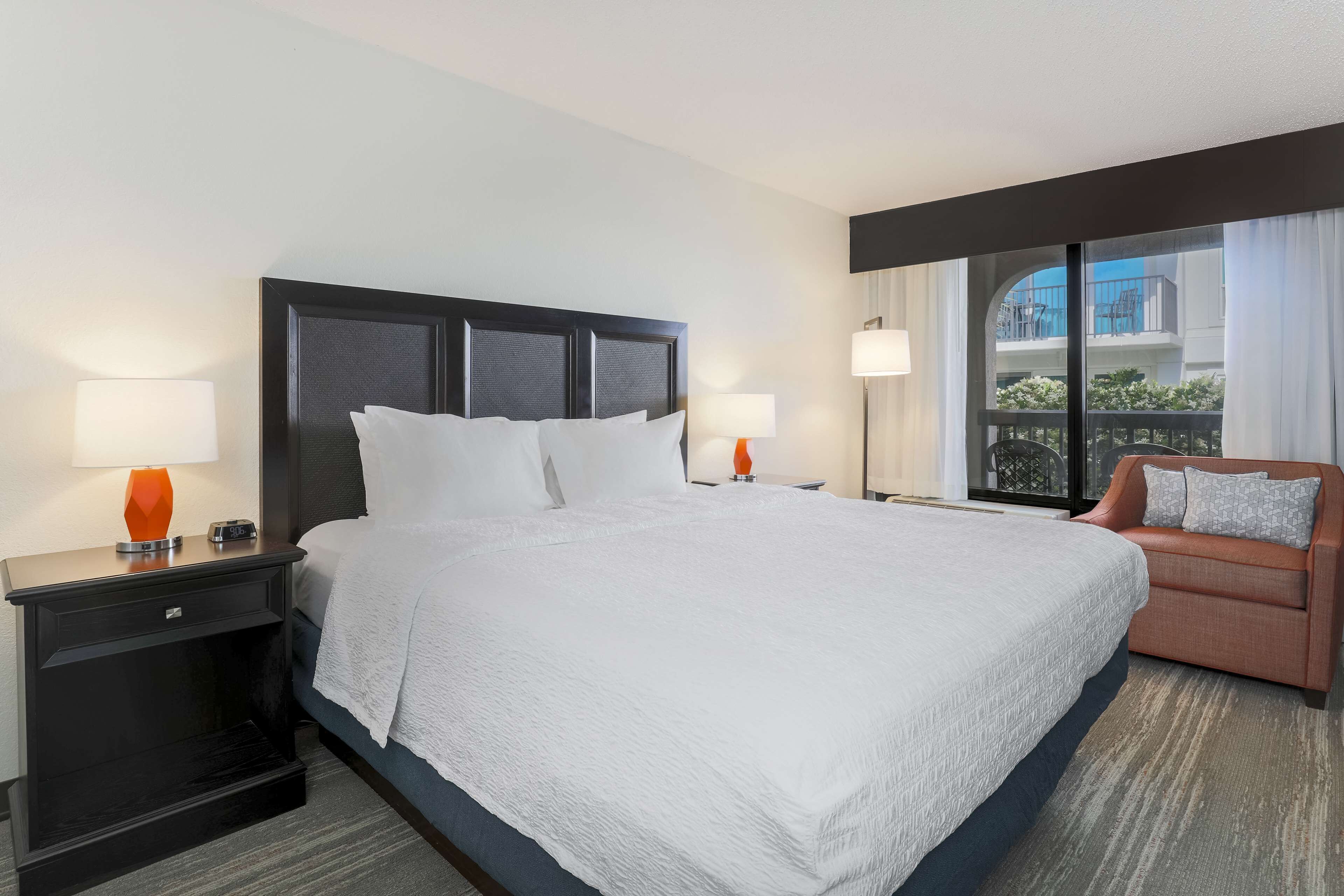 Habitación de hotel con una cama grande, dos mesitas de noche con lámparas, un sofá y vistas al balcón exterior.