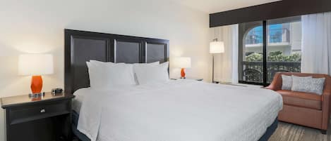 A hotel room with a large bed, two bedside tables with lamps, a sofa, and a view of the outside balcony.