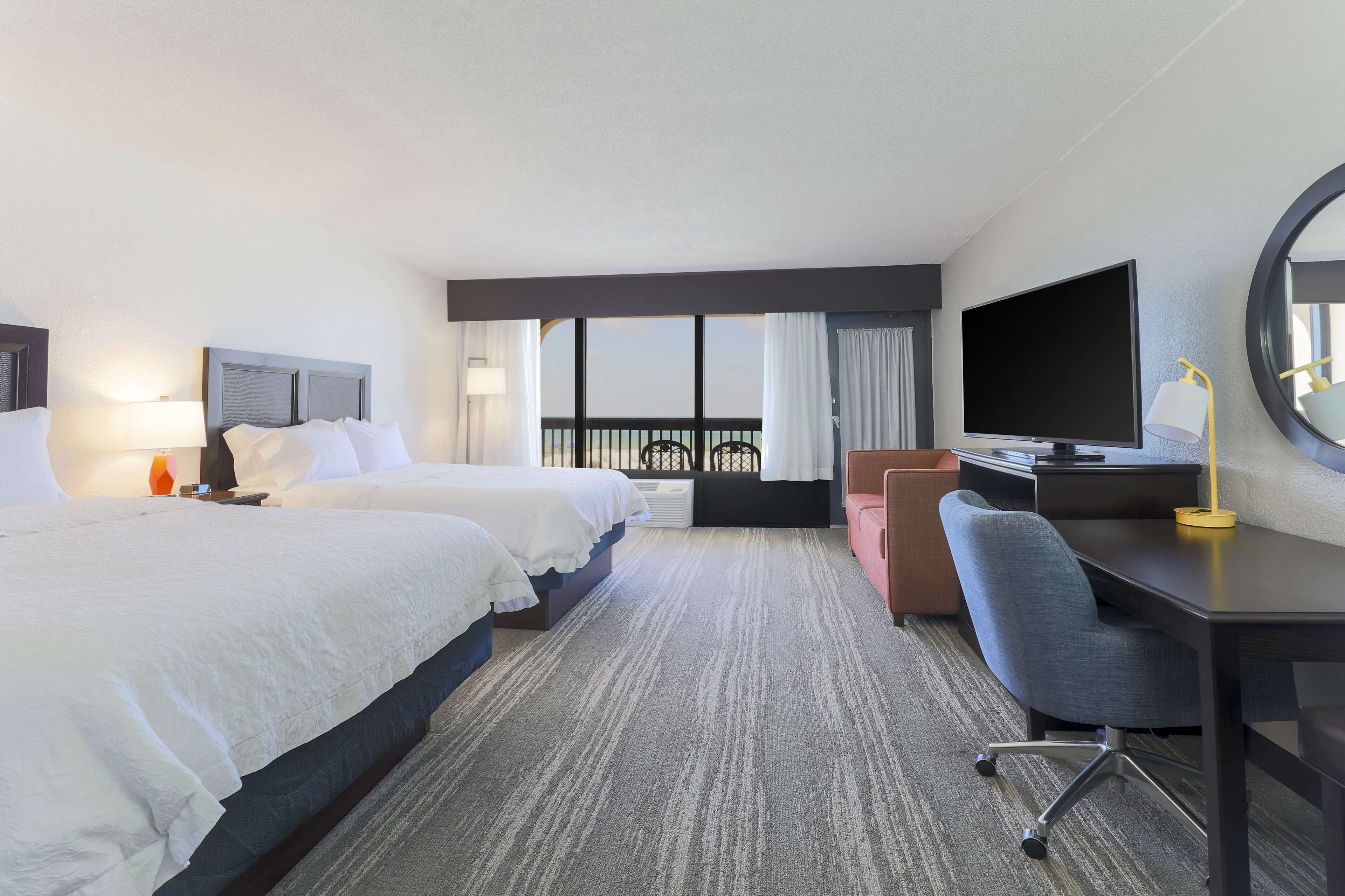 Une chambre d’hôtel avec deux lits, un bureau avec une chaise, une télévision et une grande fenêtre avec des rideaux.