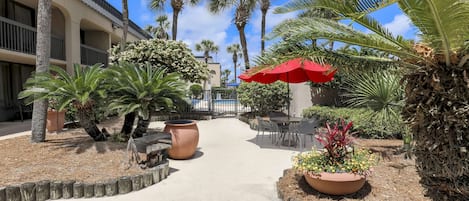 A courtyard with palm trees, outdoor seating, and a red umbrella.