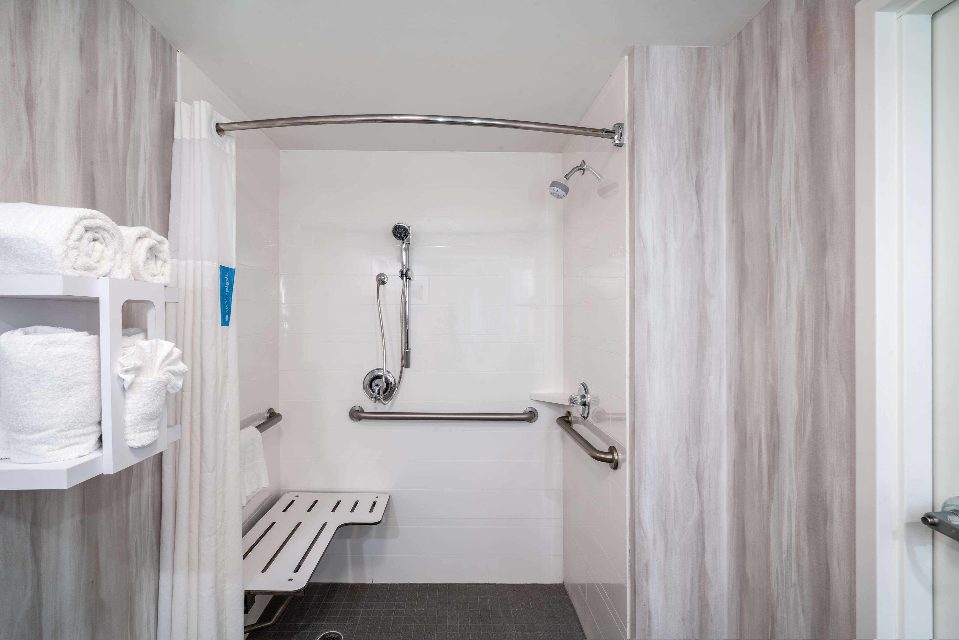 Een moderne badkamer met douche, handgrepen, een handdoekhouder en een bankje.