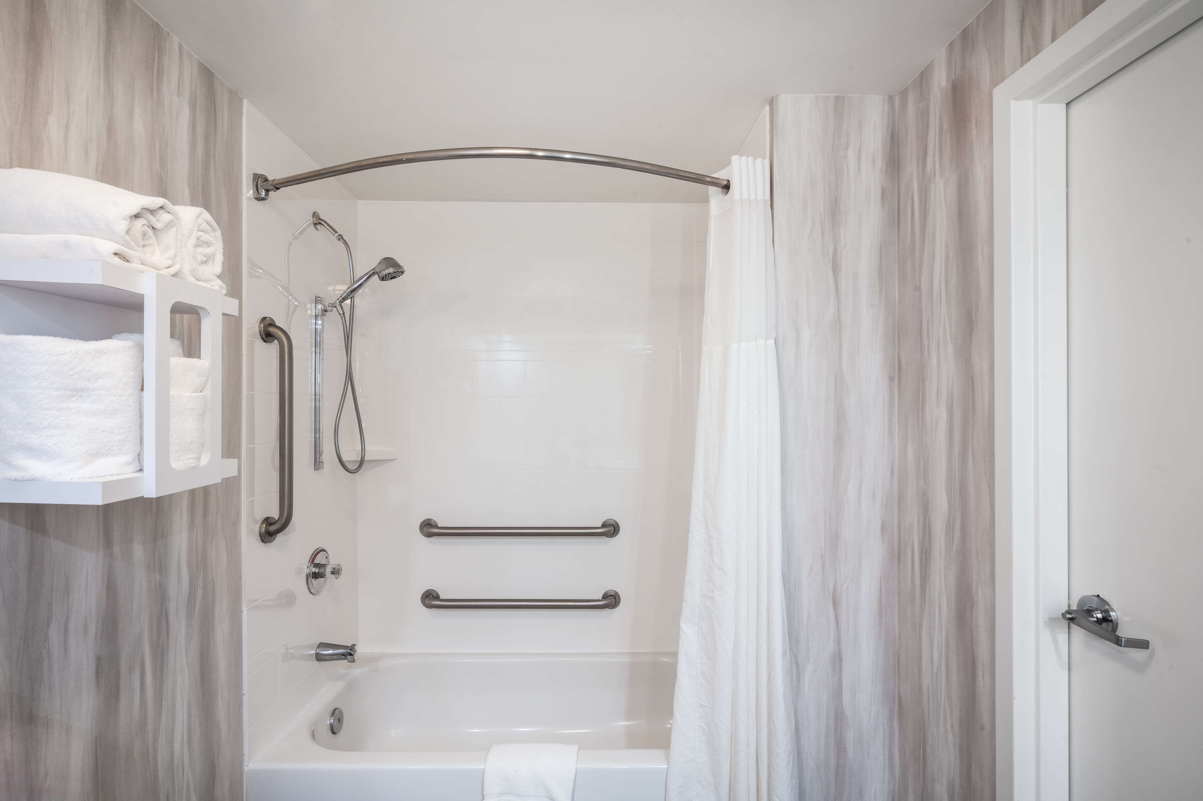 A modern bathroom with a walk-in shower, grab bars, a towel rack, and a white bathtub.