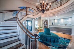 A grand staircase with a wooden handrail and white balusters, leading to a second floor. A chandelier hangs from the ceiling, and a sign reads "WELCOME TO THE SUN SHINE STATE". - Hampton Inn and Suites Amelia Island Historic Harbor Front (Fernandina Beach)