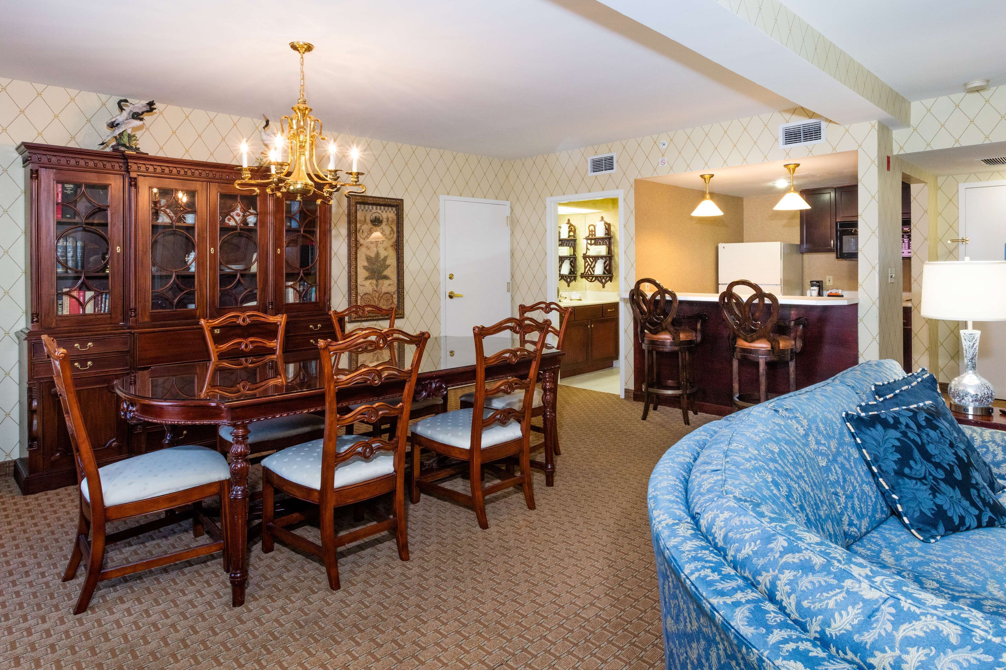 A dining area with a wooden table and chairs, a chandelier, and a blue sofa with a patterned cushion.