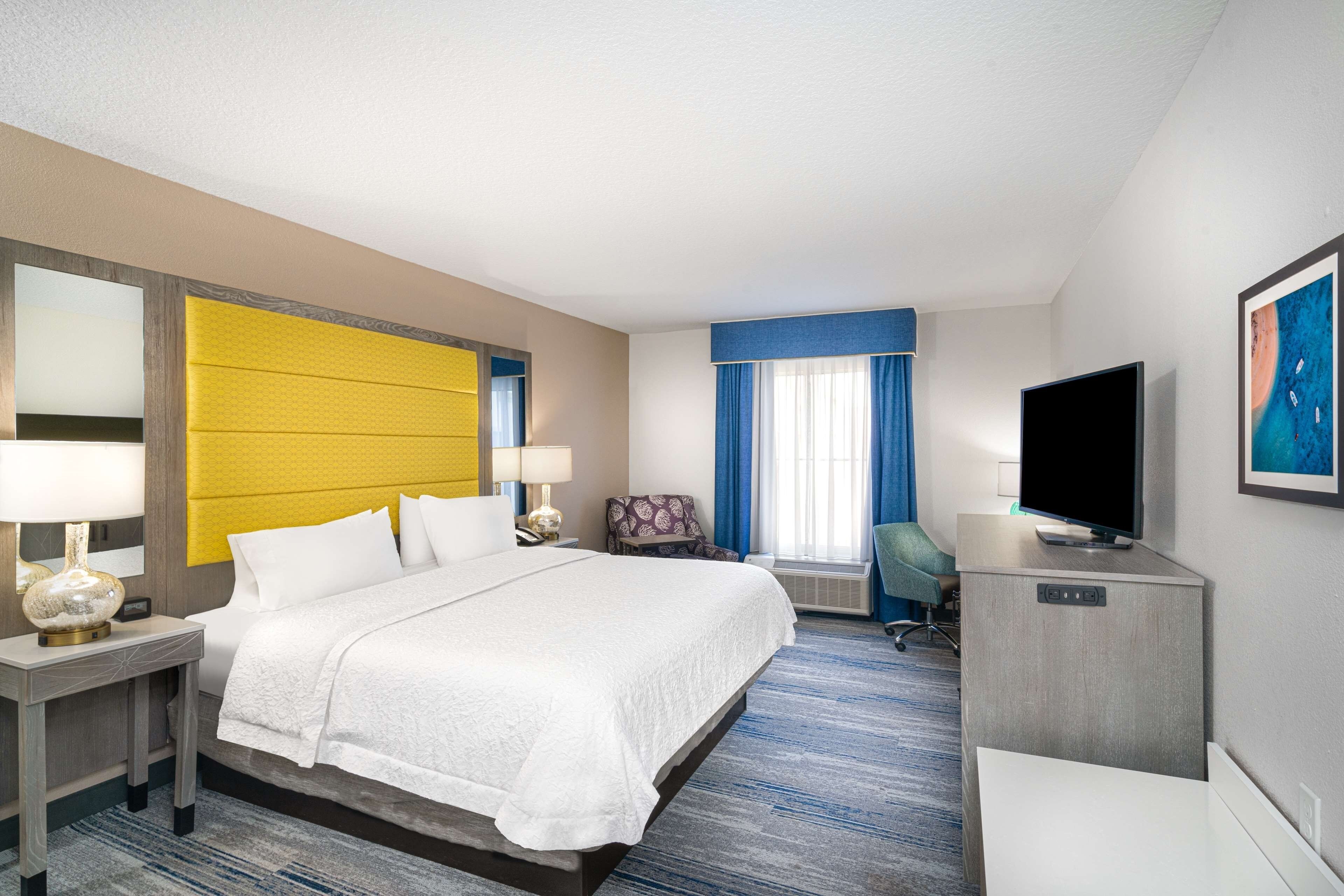 A hotel room with a large bed, a desk, a television, and a chair.