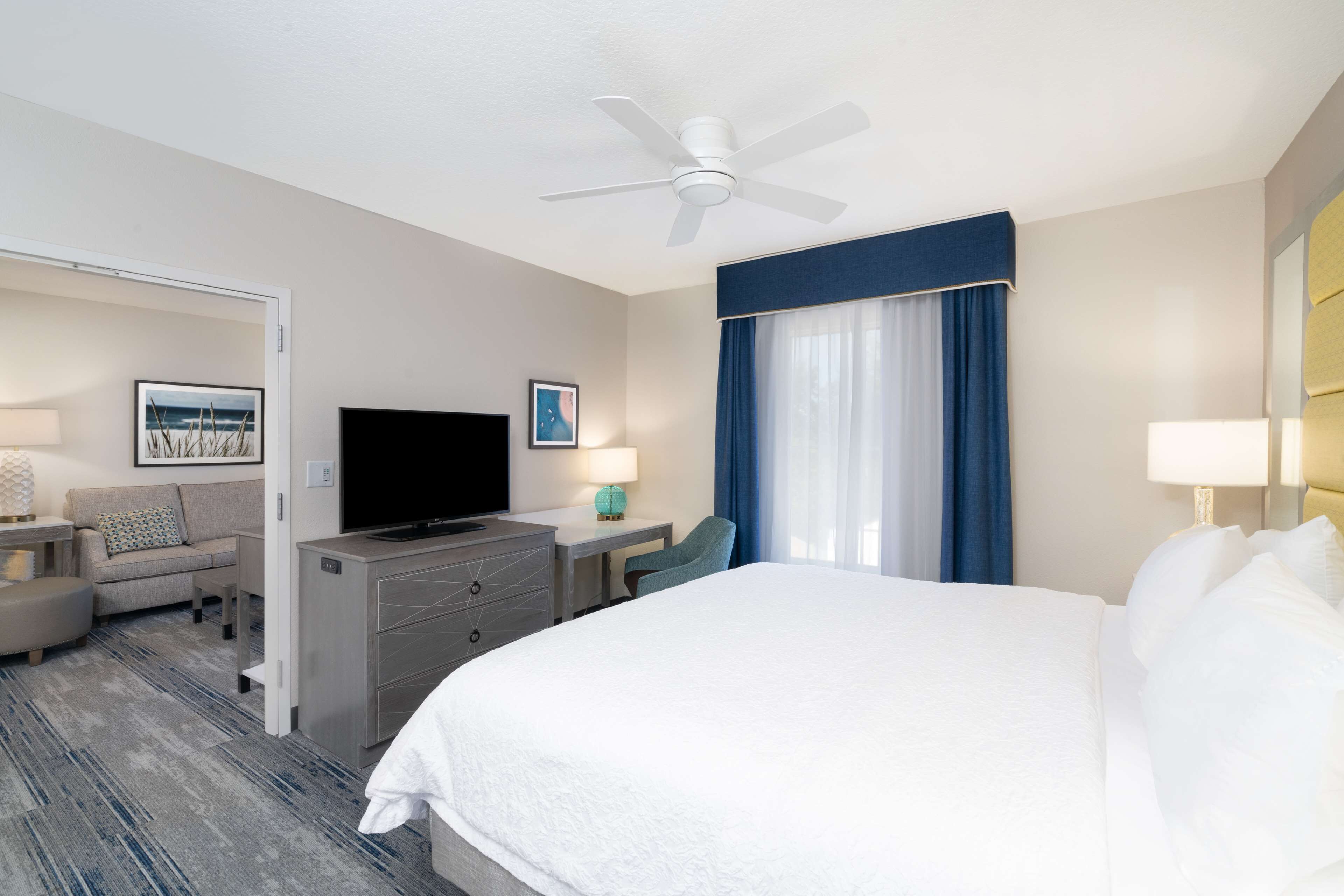 A hotel room with a bed, a desk, a television, a chair, and a ceiling fan.