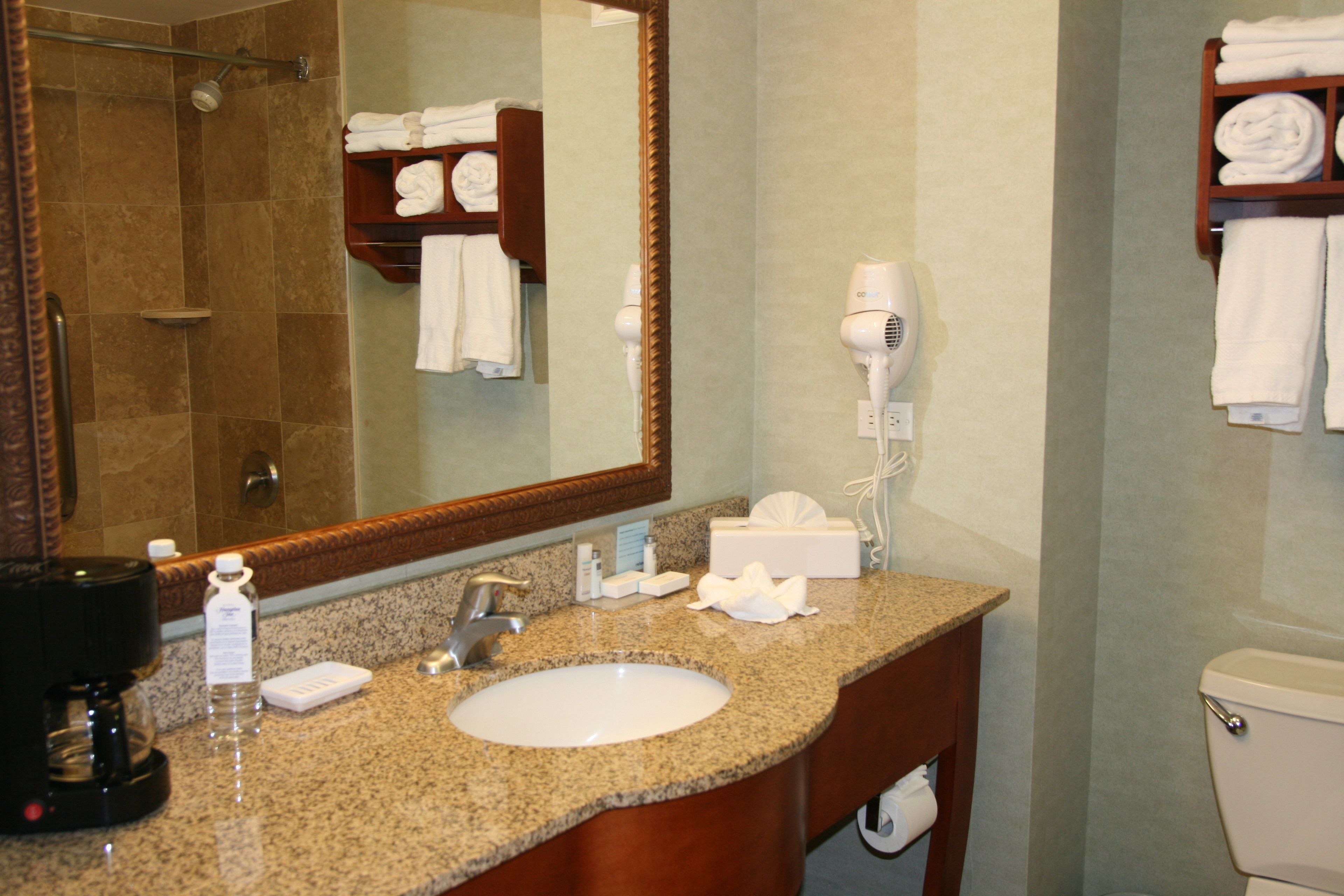 A bathroom with a granite countertop, a white sink, a mirror, a hairdryer, and a towel rack with folded towels.